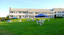 Guests enjoying leisure activities on the lawn, eating at umbrella covered tables and relaxing in lounge chairs in front of Beachmere South.