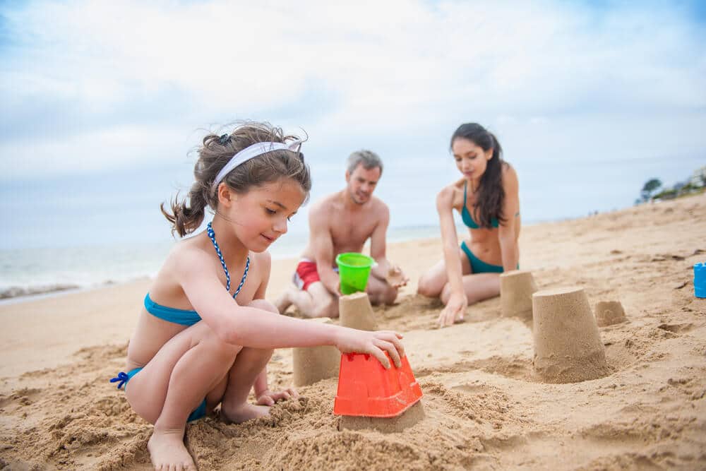 Two adults watch as a child builds a sand castle on a Ogunquit beach.